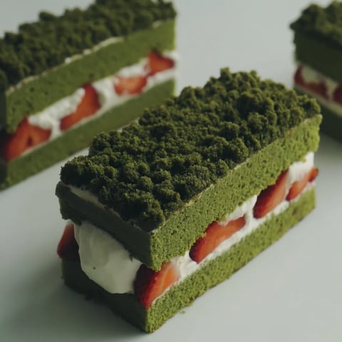 A slice of green tea cake with white cream and strawberries.
